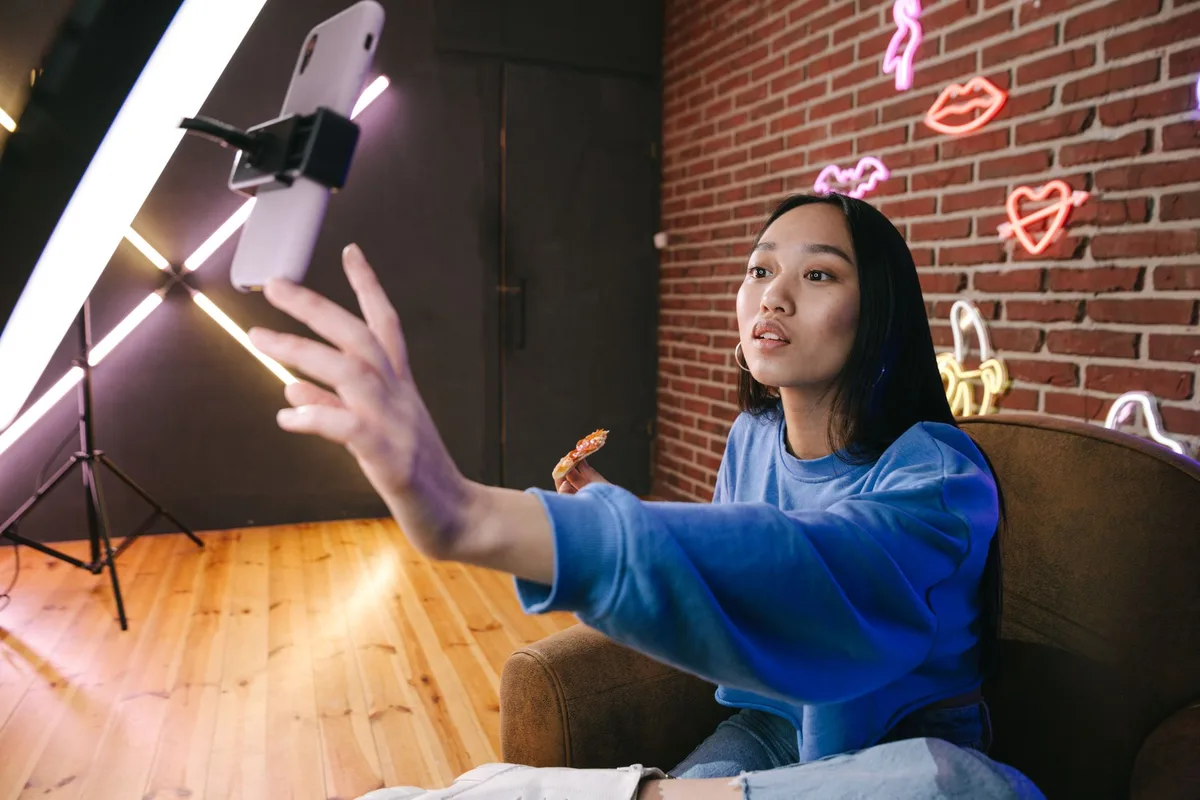 Male creator recording video content indoors using a smartphone and ring light while holding a notebook