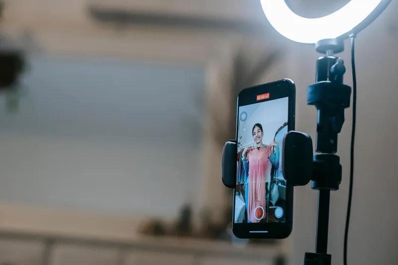 Creator wearing a beanie recording a vlog indoors using a smartphone and ring light setup