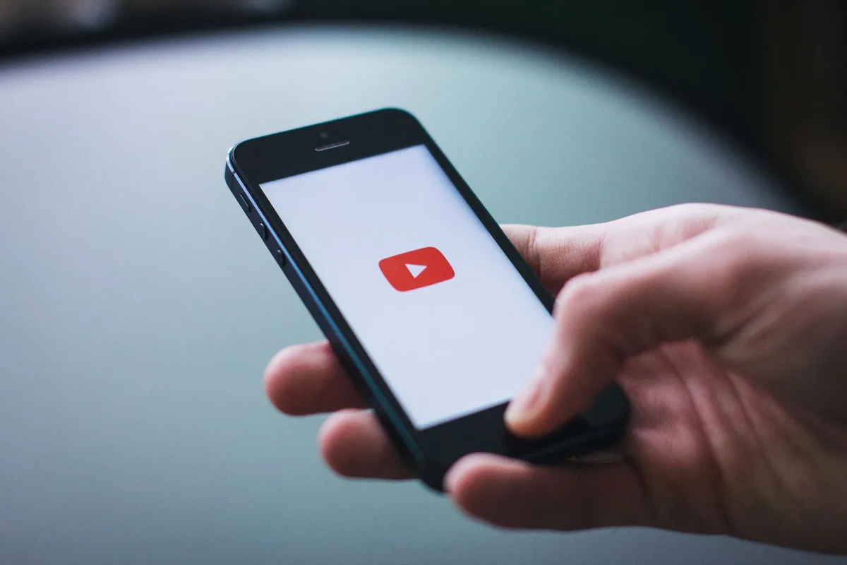 A hand holding a smartphone displaying the YouTube app against a red background